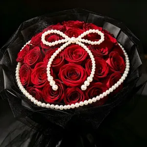 Élégant bouquet de roses rouges orné d'un nœud en perles blanches dans un filet noir.
