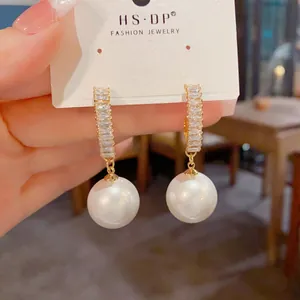 Détail de boucles d'oreilles dorées en C avec baguettes de zircone et perles pendantes