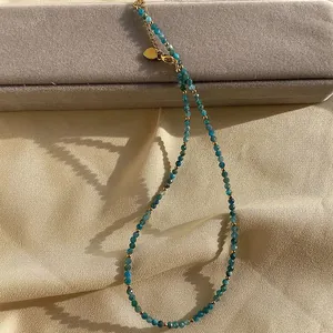 Detail view of a faceted natural stone beaded necklace with gold spacers on fabric.