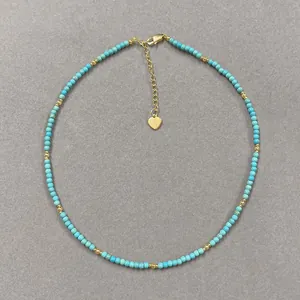 Close-up detail of handmade turquoise and gold beaded necklace with heart charm.