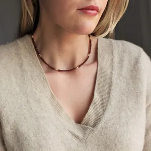 Detailed view of a delicate faceted burgundy stone necklace with gold beads on a model.