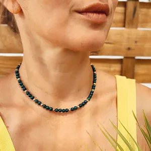 Detailed shot of a dainty green malachite necklace with gold beads on a model's neck.