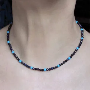 Detail of handmade faceted natural black and light blue stone beaded necklace worn on neck.
