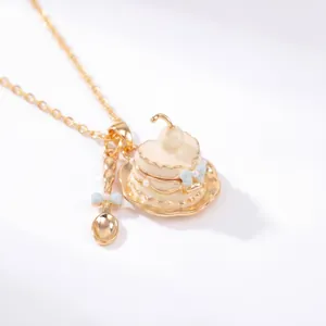 Detalle de un collar de taza de té chapado en oro con colgante que se abre y cuchara.