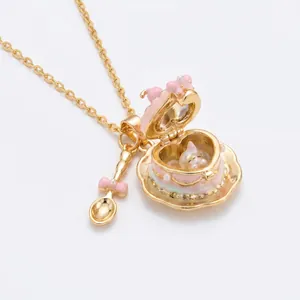 Primer plano de un colgante de taza de corazón dorado con lazo rosa y cucharilla