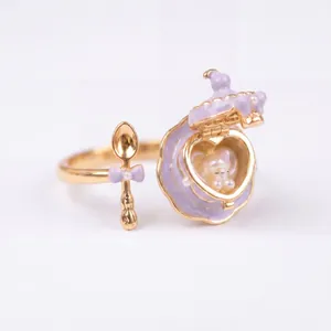 Detalle de anillo bañado en oro con una taza de té que se abre y una cuchara esmaltada.