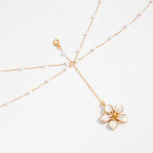 Detailed view of elegant gold body chain featuring a white flower pendant and pearls.