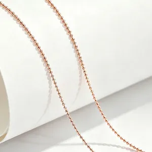 Close-up detail of rose gold titanium steel ball chain necklace on white background