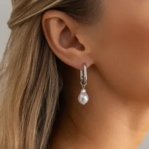 Close-up detail showing a silver U-shaped link earring with a white baroque pearl pendant worn