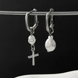 Close-up of asymmetric silver hoop earrings with baroque pearls and a cross charm