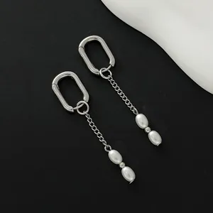 Close-up of silver U-shaped earrings with delicate chain tassels and oval white pearls.