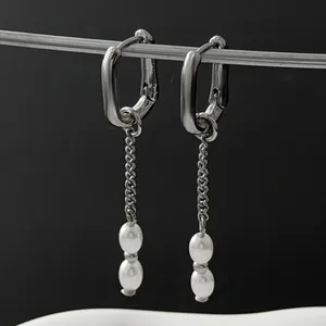 Detailed macro view of silver U-shaped hoop earrings featuring dangling chains and white pearls.