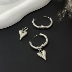 Detailed view of silver hoop earrings with detachable heart pendants on black background