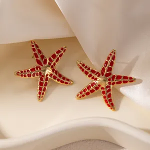 Détail de boucles d'oreilles étoile de mer en émail rouge sur fond satiné blanc