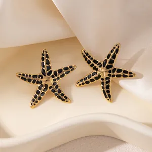 Gros plan de boucles d'oreilles étoile de mer en acier doré avec taches en émail noir
