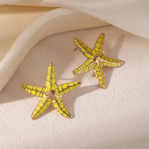 Gros plan de boucles d'oreilles étoile de mer dorées avec motif émail vert citron vif.
