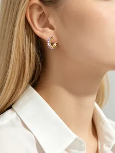 Detailed close-up showing gold hoop earrings featuring square purple cubic zirconia