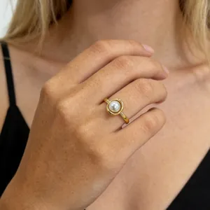 Close-up of an elegant gold titanium steel ring featuring a white pearl on a woman's finger