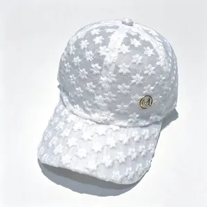 Détail d'une casquette de baseball en dentelle blanche avec badge doré logo M