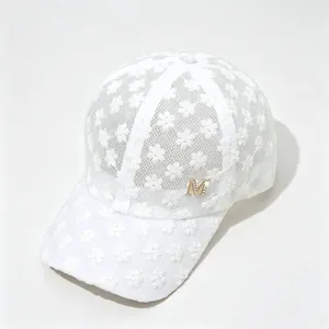 Détail d'une casquette en dentelle fleurie blanche avec emblème M en strass dorés