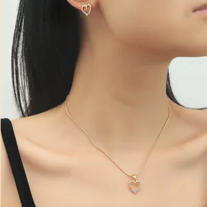 Close-up of model wearing gold heart-shaped necklace and matching zircon earrings