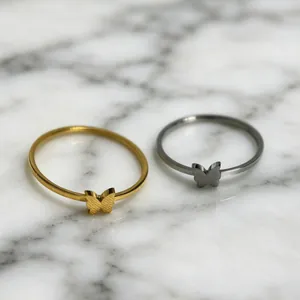 Primer plano detallado de anillos de mariposa minimalistas en oro y plata sobre mármol