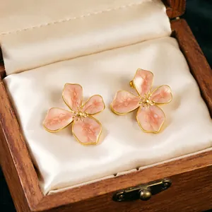Macro view of pink enamel cherry blossom stud earrings presented in a wooden gift box