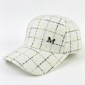 Détail d'une élégante casquette de baseball en tweed avec logo M métallique et carreaux.