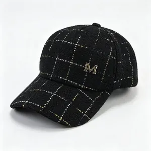 Détail d'une casquette de baseball en tweed noir avec un logo métallique M doré