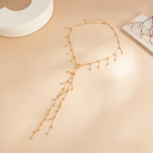 Gros plan sur un collier doré en Y avec des chaînes à pampilles délicates et des perles.