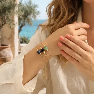 Nahaufnahme von drei 18K vergoldeten verstellbaren Armbändern mit Natursteinperlen am Handgelenk