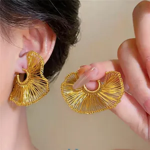 Primer plano de elegantes pendientes dorados en forma de abanico en la oreja en detalle.