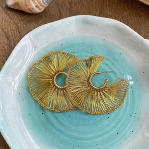 Pendientes de aro de hilo dorado hechos a mano presentados en un plato azul