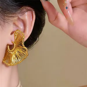 Detalle de pendientes dorados trenzados en forma de abanico puestos en la oreja.