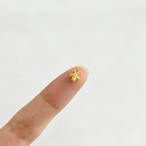Petit pendentif fleur en acier inoxydable doré sur le bout du doigt pour échelle.