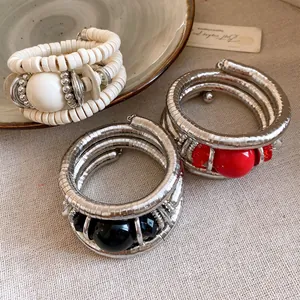 Close-up detail of multilayer metallic wrap bracelets with red and black acrylic beads
