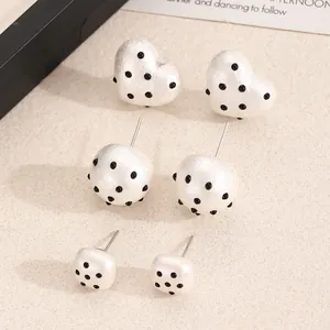 Detail of white acrylic earrings with black polka dots in heart and round shapes.