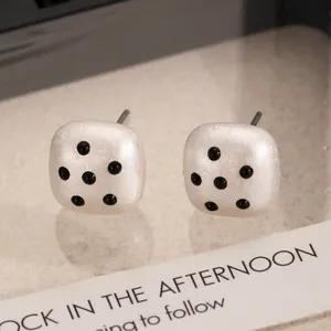 Detailed macro view of white square acrylic stud earrings with black polka dot pattern