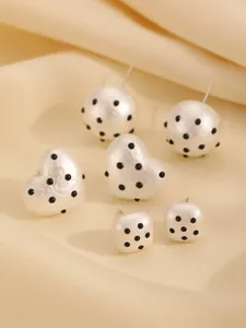 Detail view of white heart and sphere stud earrings with black polka dot textured finish