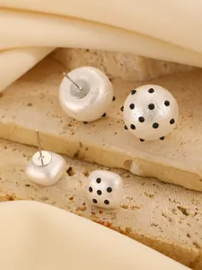 Detailed macro view of white acrylic stud earrings featuring decorative black polka dot patterns
