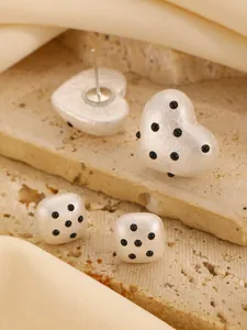 Detail of white heart and cube earrings with black polka dots on stone background