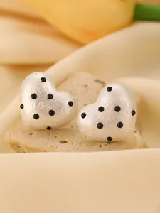 Close-up of white heart-shaped earrings with black polka dots and textured finish