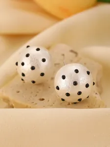 Detailed view of spherical white stud earrings with raised black polka dot patterns