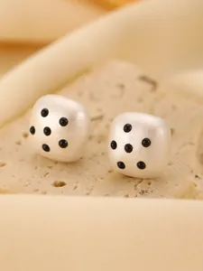 Macro view of minimalist matte white dice-shaped stud earrings with black polka dot design