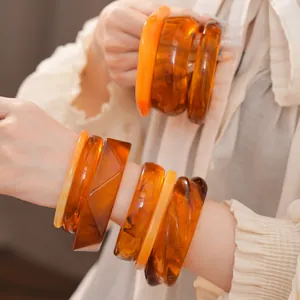 Gros plan de bracelets géométriques élégants en résine ambre et orange portés au poignet.