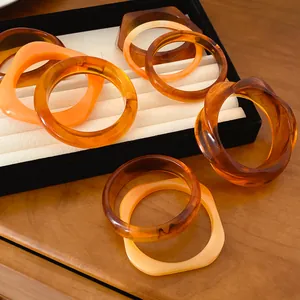 Gros plan détaillé de bracelets en résine géométriques en tons ambre et orange sur un plateau