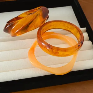 Détail de trois bracelets géométriques en résine avec texture écaille d'ambre sur un plateau