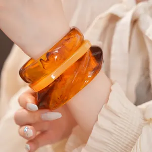 Vue détaillée de bracelets en résine ambrée aux motifs écailles sur le poignet d'un modèle