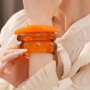 Gros plan de bracelets en résine irréguliers en ambre et orange sur un poignet.