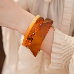 Vue détaillée de bracelets en résine ambre géométriques sur le poignet d'une femme élégante